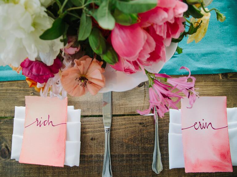 Two pink escort cards sit next to each other at a place setting