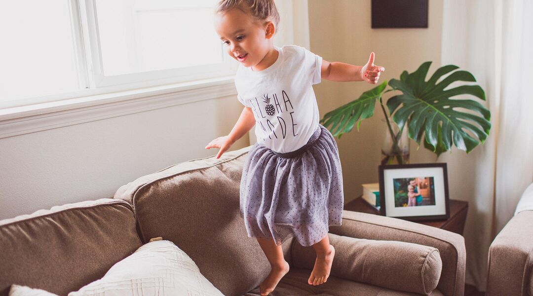 happy little girl jumping on the couch at home