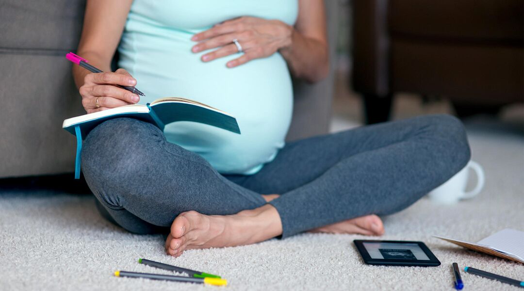 Pregnant woman sitting cross-legged, writing in journal