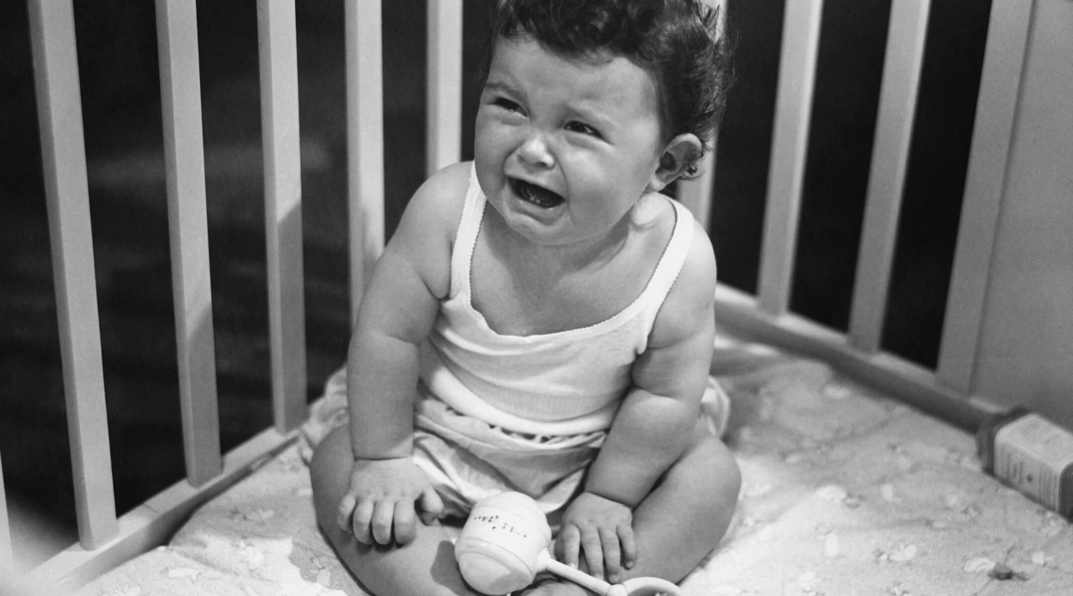 Retro black and white photo of baby crying in playpen. 