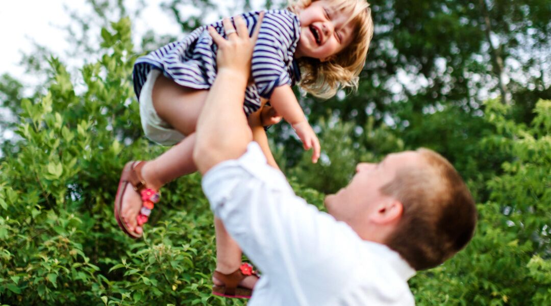 Dad holding up giggling toddler girl in the air.