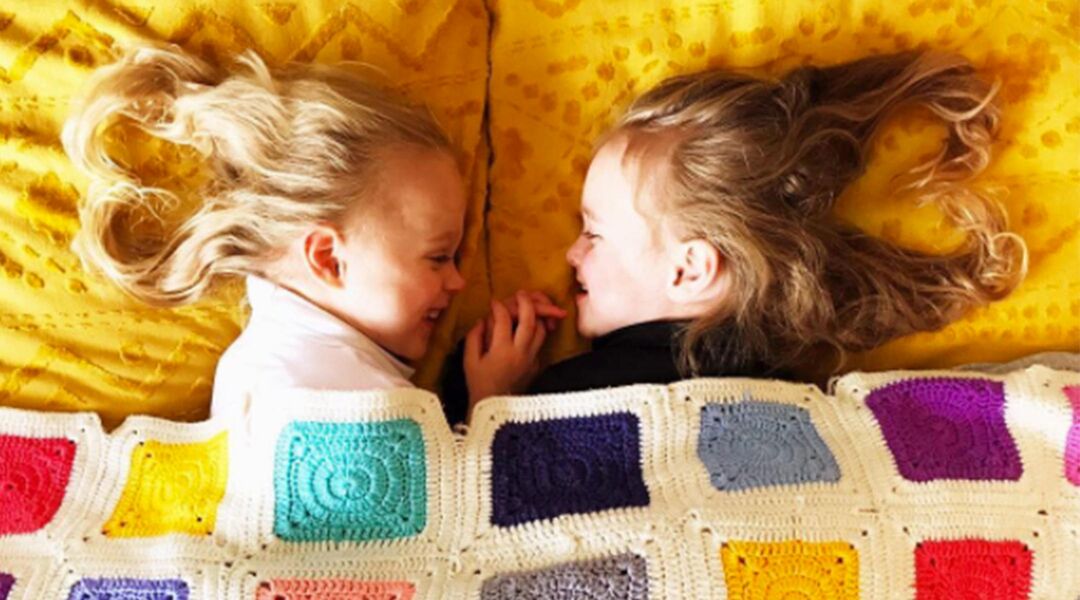 Twin girls facing each other under quilt