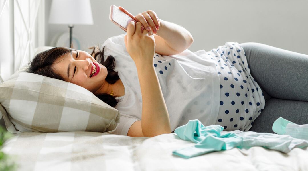 pregnant woman laughing bed looking mobile phone