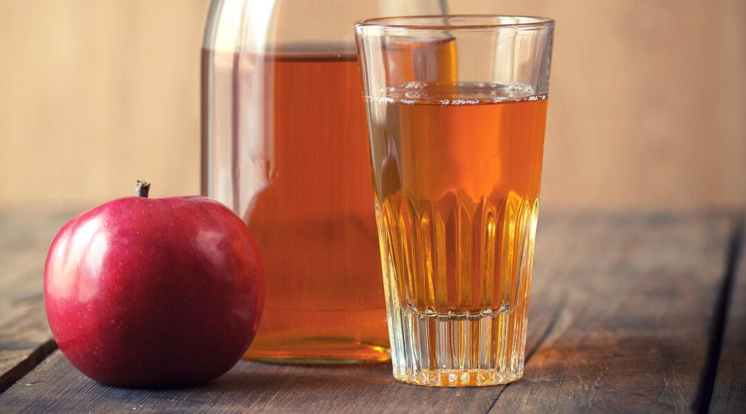Glass of apple juice with jug on wooden surface. 
