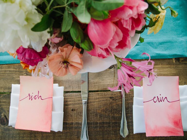 Two pink escort cards sit next to each other at a place setting