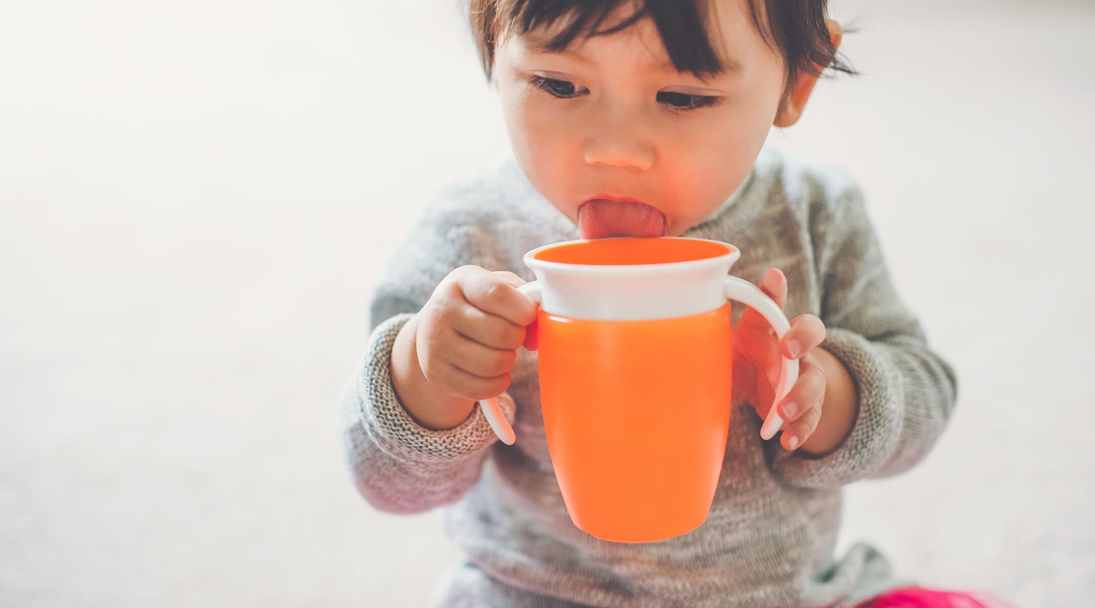 toddler drinking from orange sippy cup