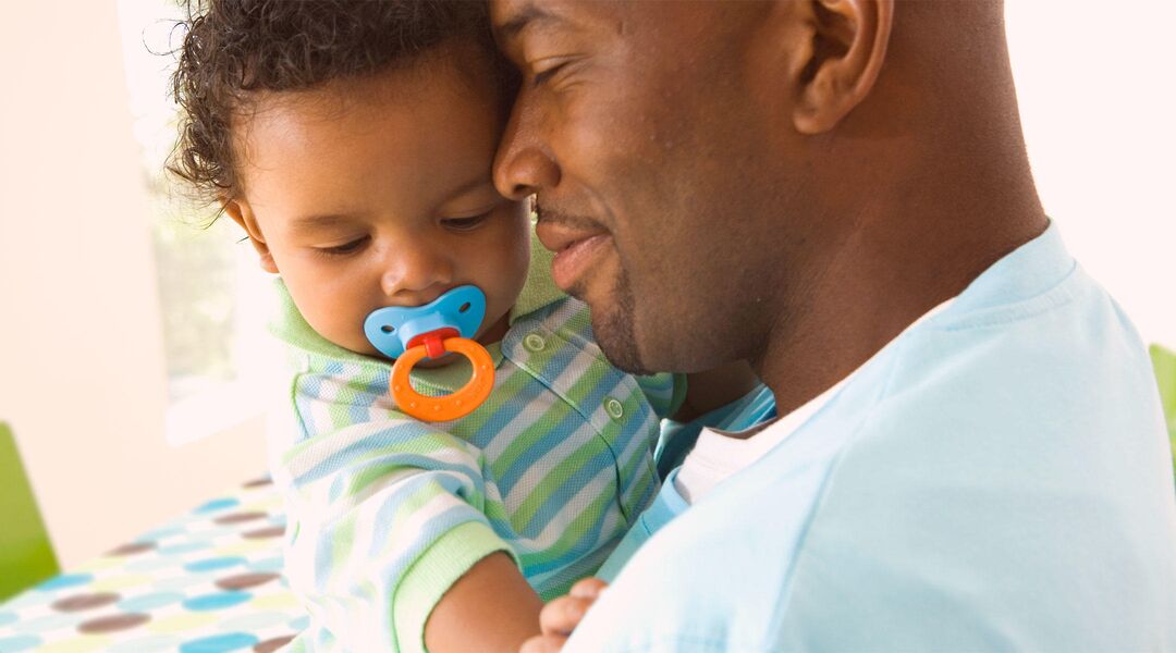 Close-up of father embracing toddler who is using a pacifier.