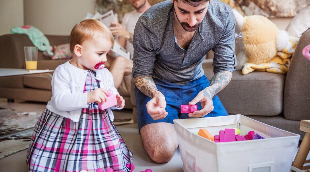 Same sex couple at home playing blocks with baby girl. 