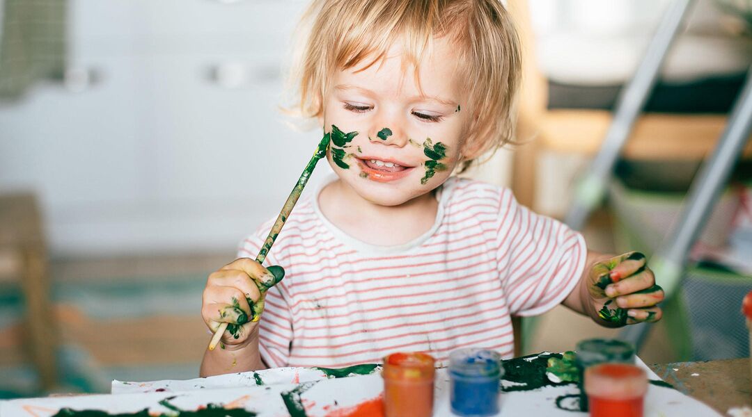 Child painting his own face in green