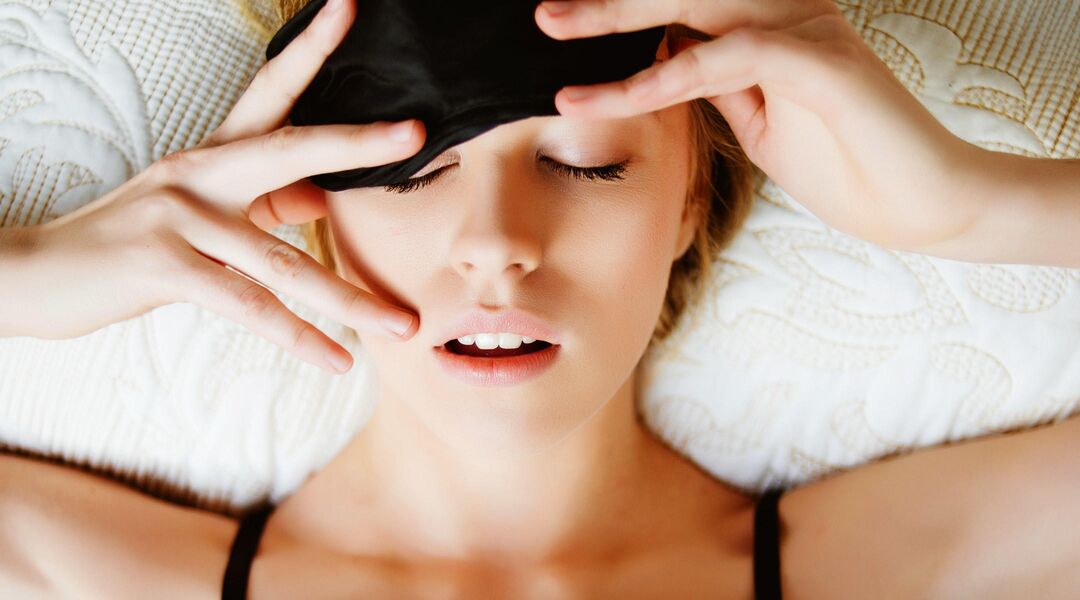Tired woman in bed waking up and removing eye mask. 