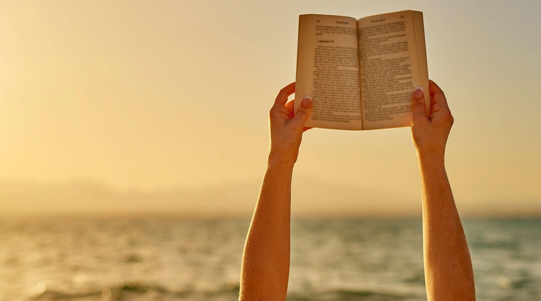 hands holding book up at beach