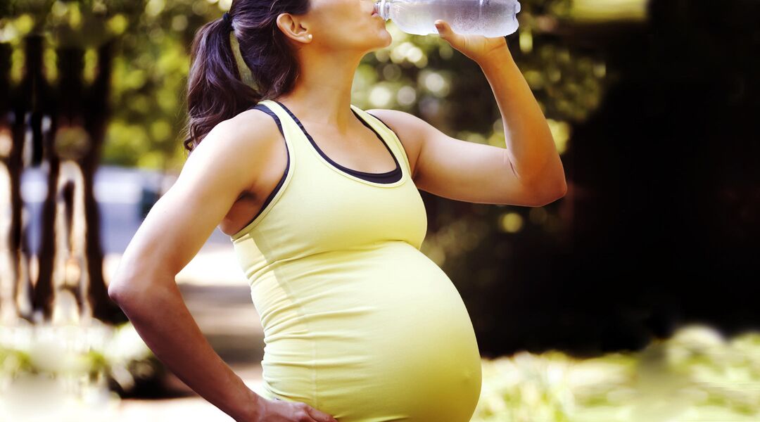pregnant woman exercising outside drinking water bottle