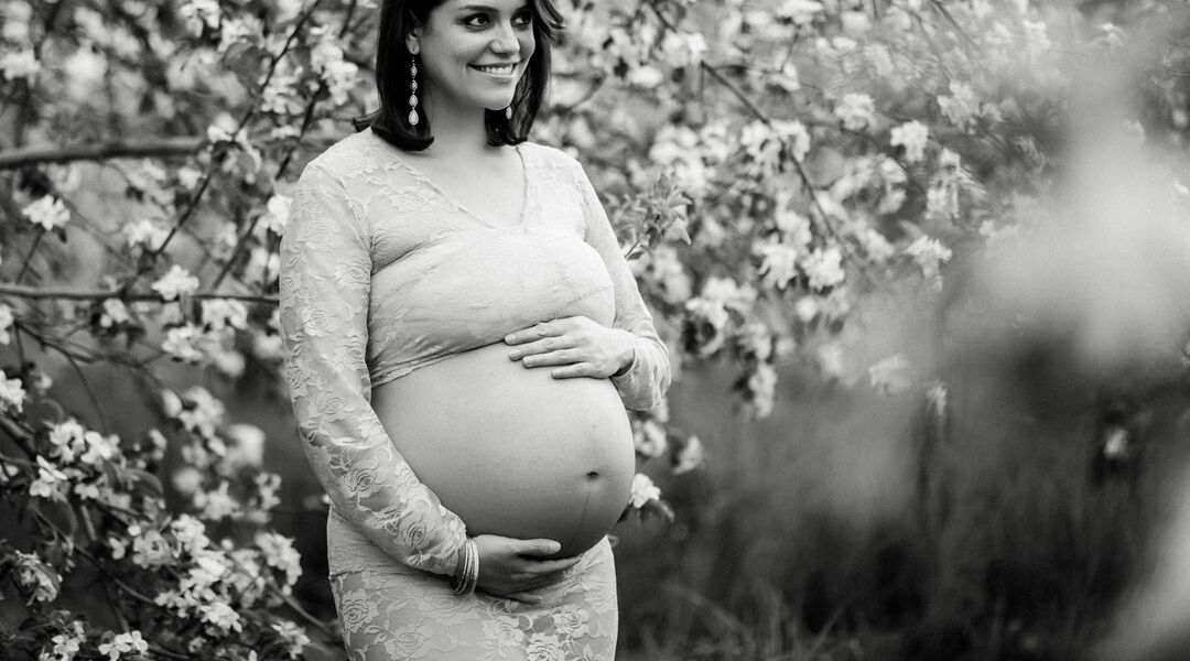 Black and white photo of woman posing for maternity shoot among apple blossoms. 