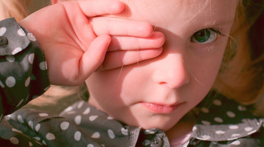 sad little girl covering her pink eye