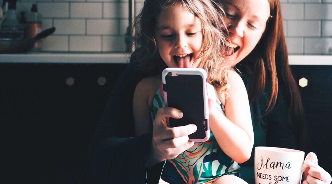 mom and toddler daughter at home, viewing video on phone
