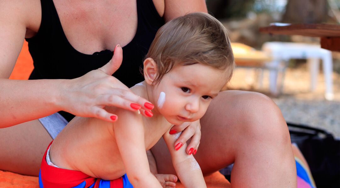 mother putting sunscreen on toddler boy