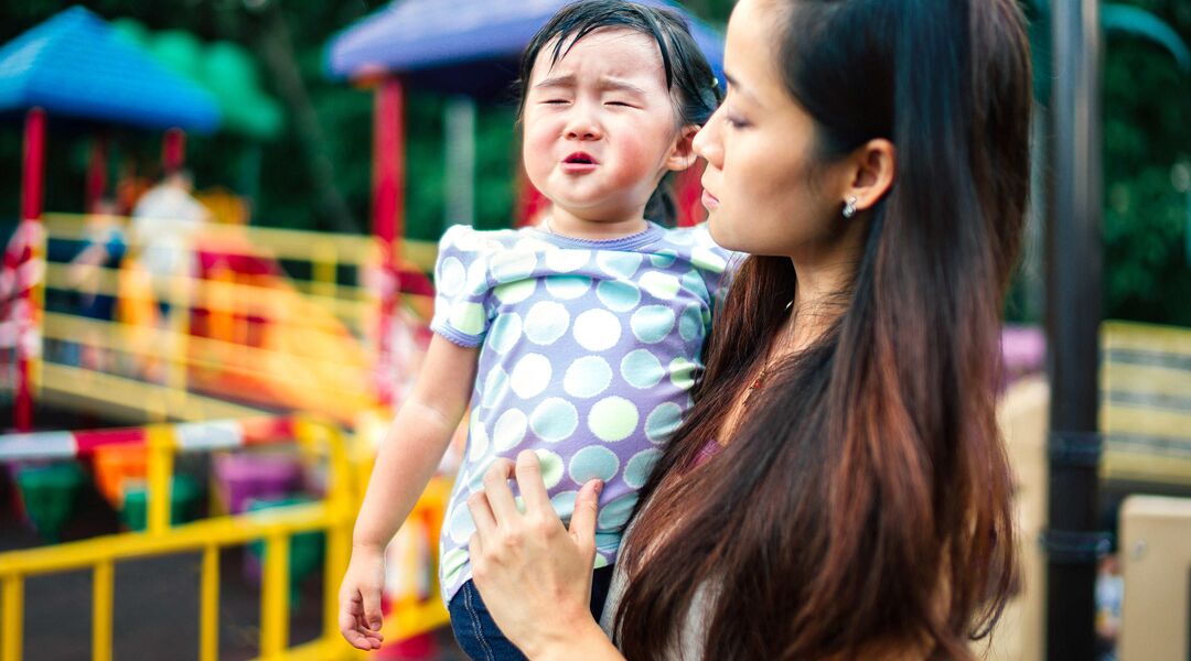 mom holding toddler having tantrum at playground