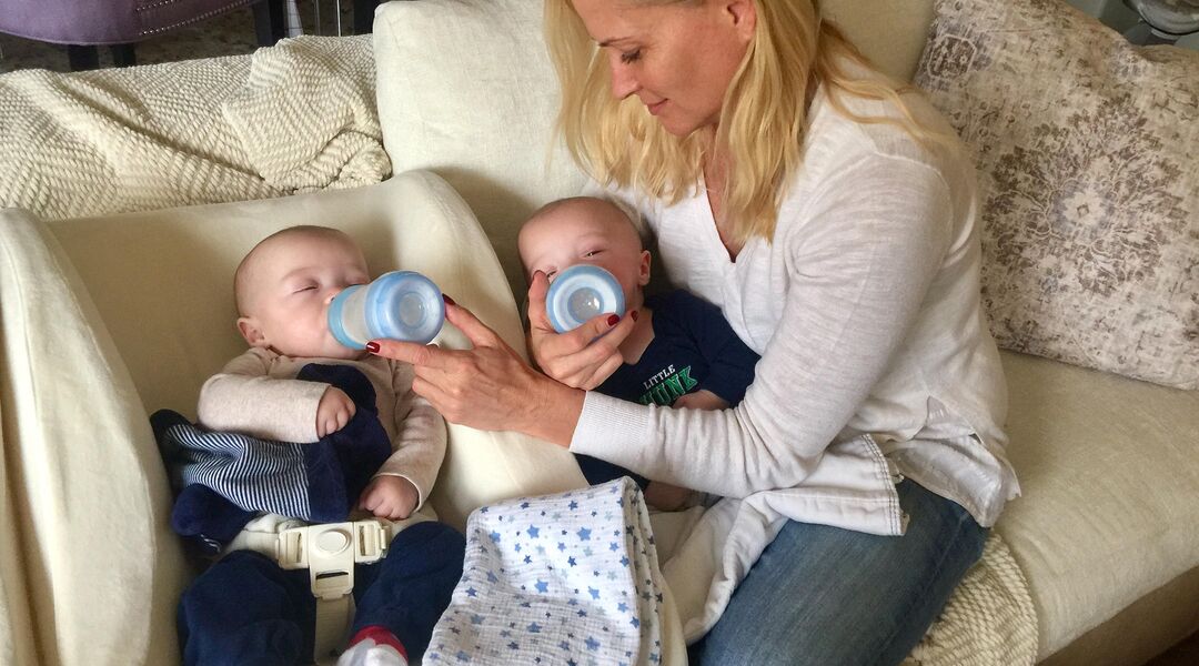 Mom bottle feeding twin boys on couch