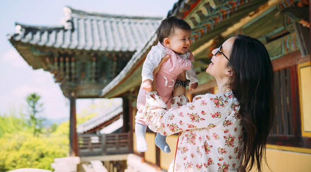mom lifting baby into the air while traveling in country with asian temple