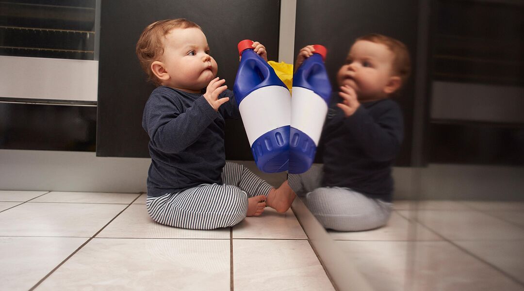 baby clutching bleach bottle from under sink