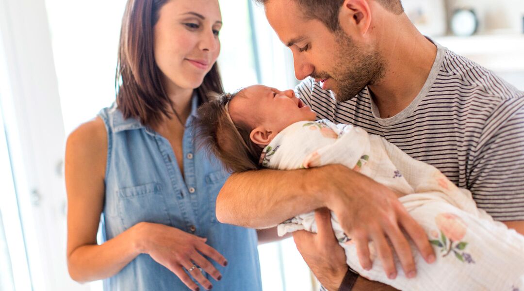Dad holding crying baby with partner nearby. 