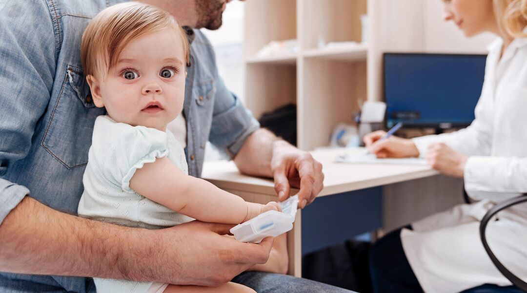wide-eyed baby sitting in dad's lap at doctor's appointment
