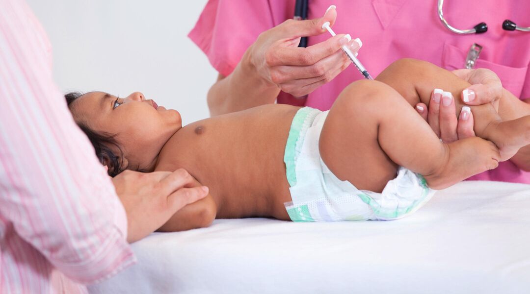 Baby in diaper at doctor's office getting vaccine in leg.
