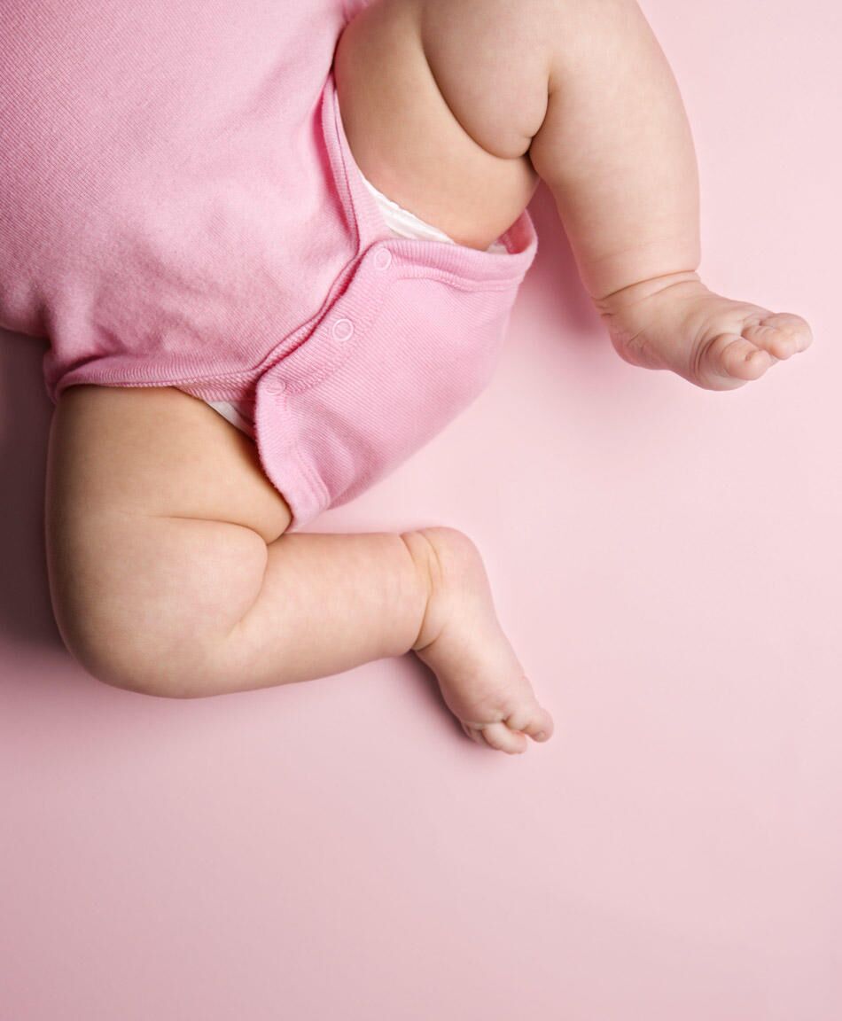 Closeup of mother hands holding cute tiny baby feet, showing baby foot.  Pink Background. Horizontal. Stock Photo