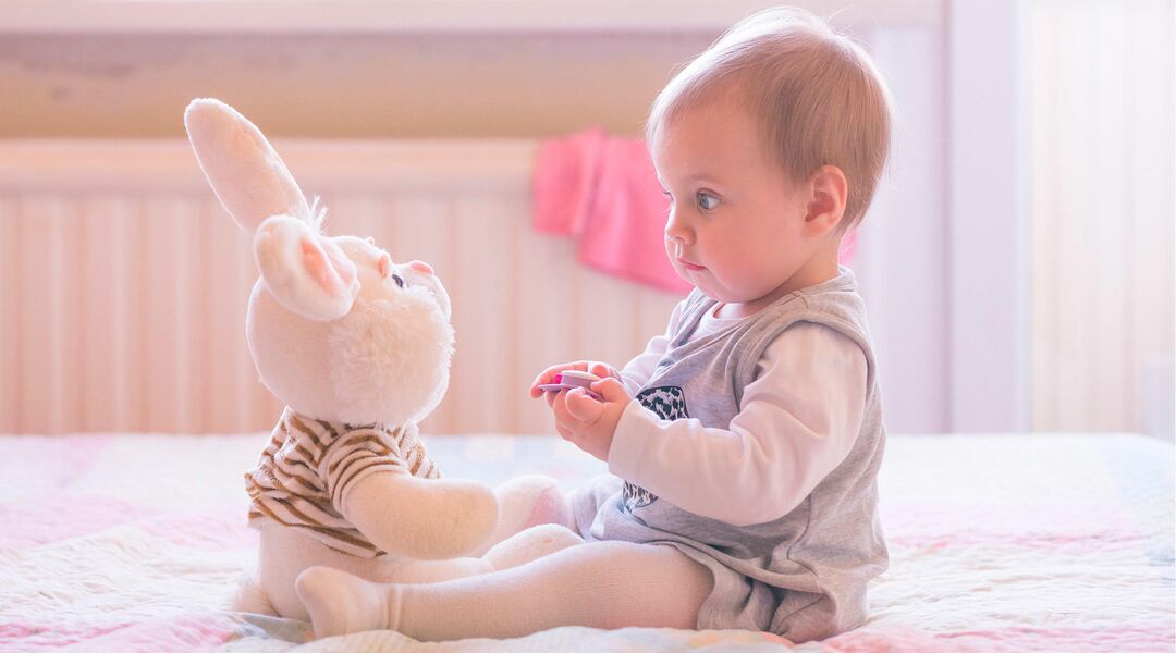 baby on bed sitting across from a stuffed animal bunny