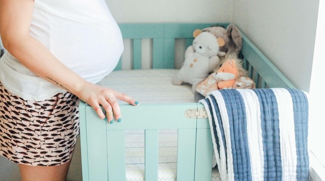 pregnant woman with belly hanging over baby's crib